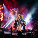 Female singer performing on stage with dancers and colorful lighting