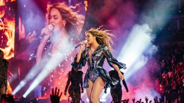 Female singer performing on stage with dancers and colorful lighting